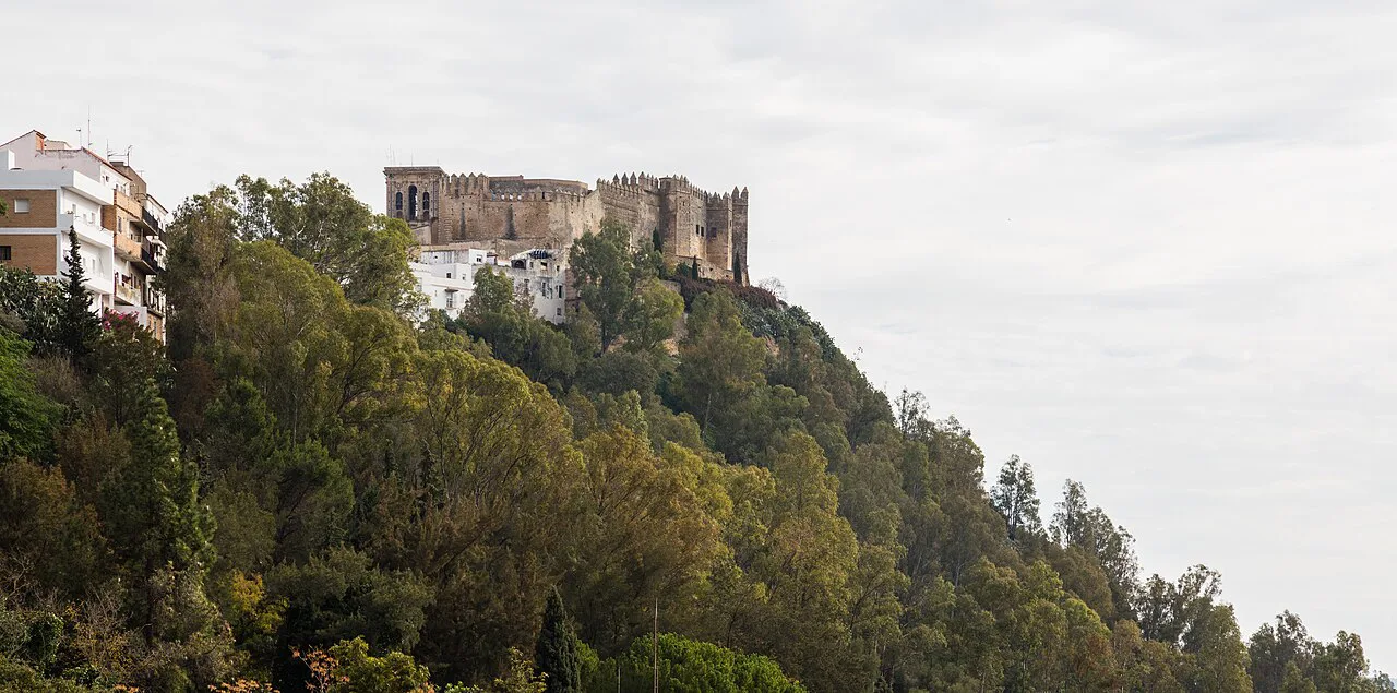 The castle of Arcos de la Frontera above the wooded cliff.