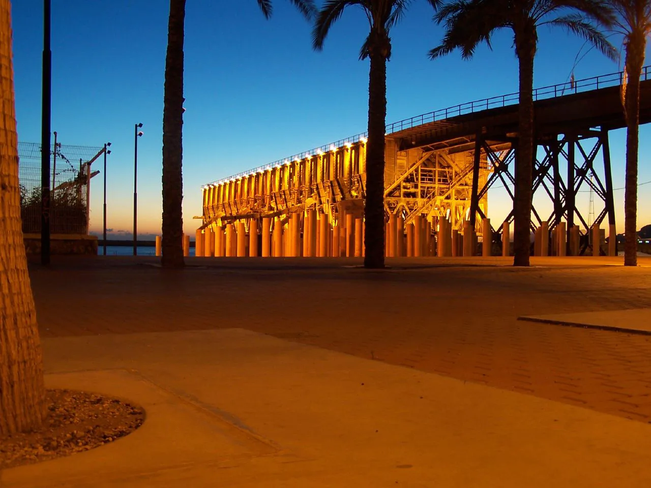 The Cable Inglés in Almería lit up at dusk, framed by palms.