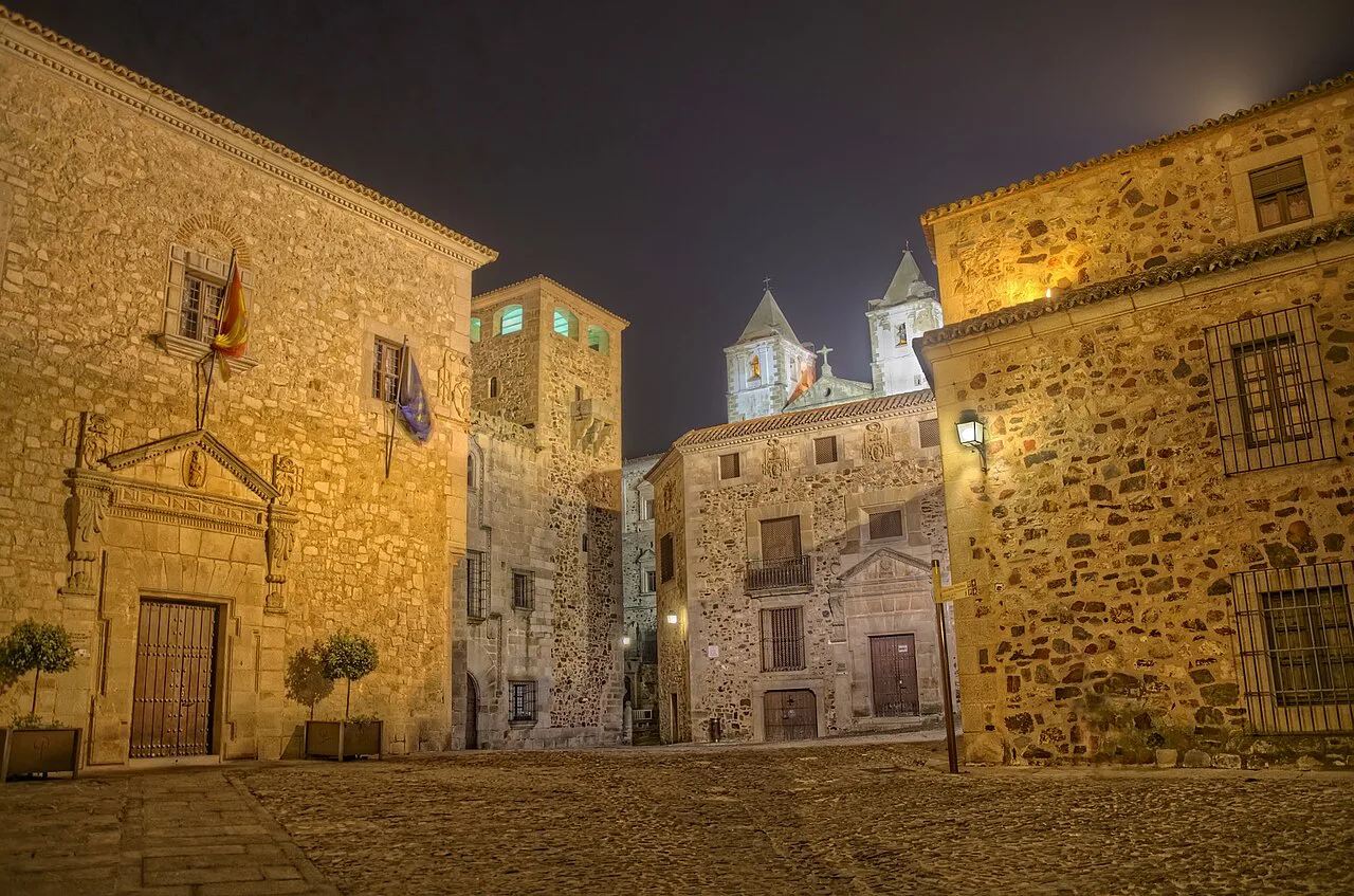 Floodlit stone streets of Cáceres old town at night.