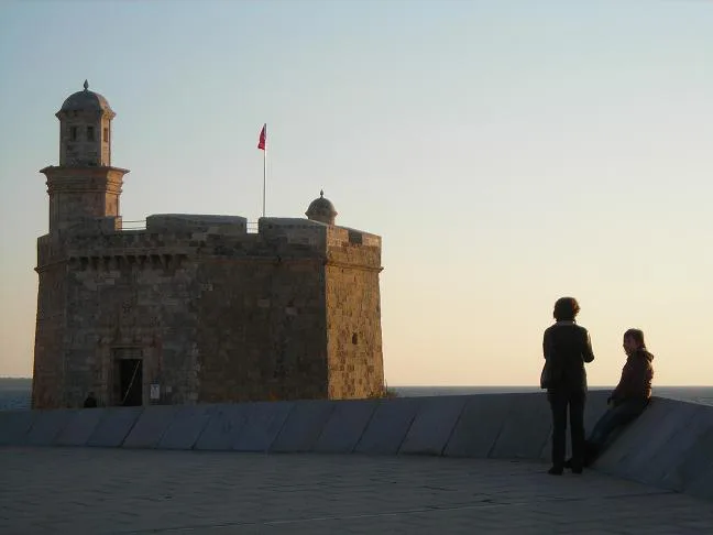 Castell de Sant Nicolau at dusk, with visitors on the waterfront, Ciutadella.