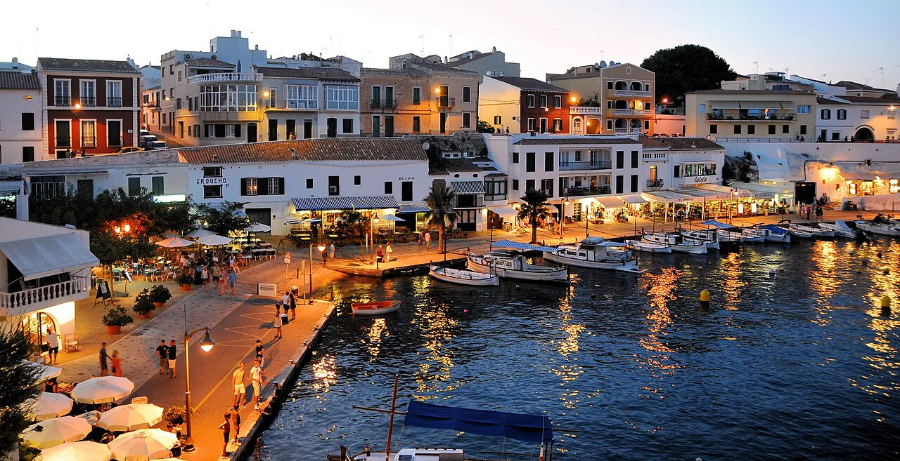 Harbourside restaurants lit at dusk in Menorca.