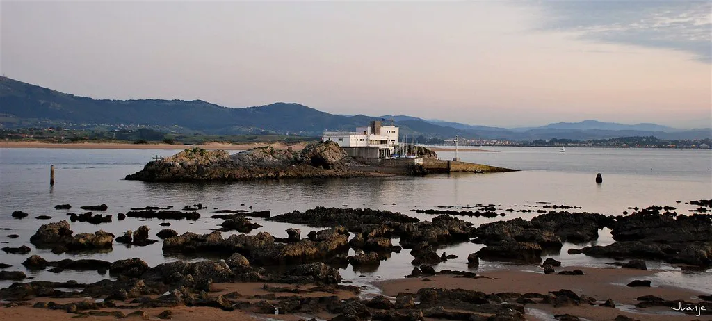 A rocky shore and islet in the Bay of Santander at dusk.