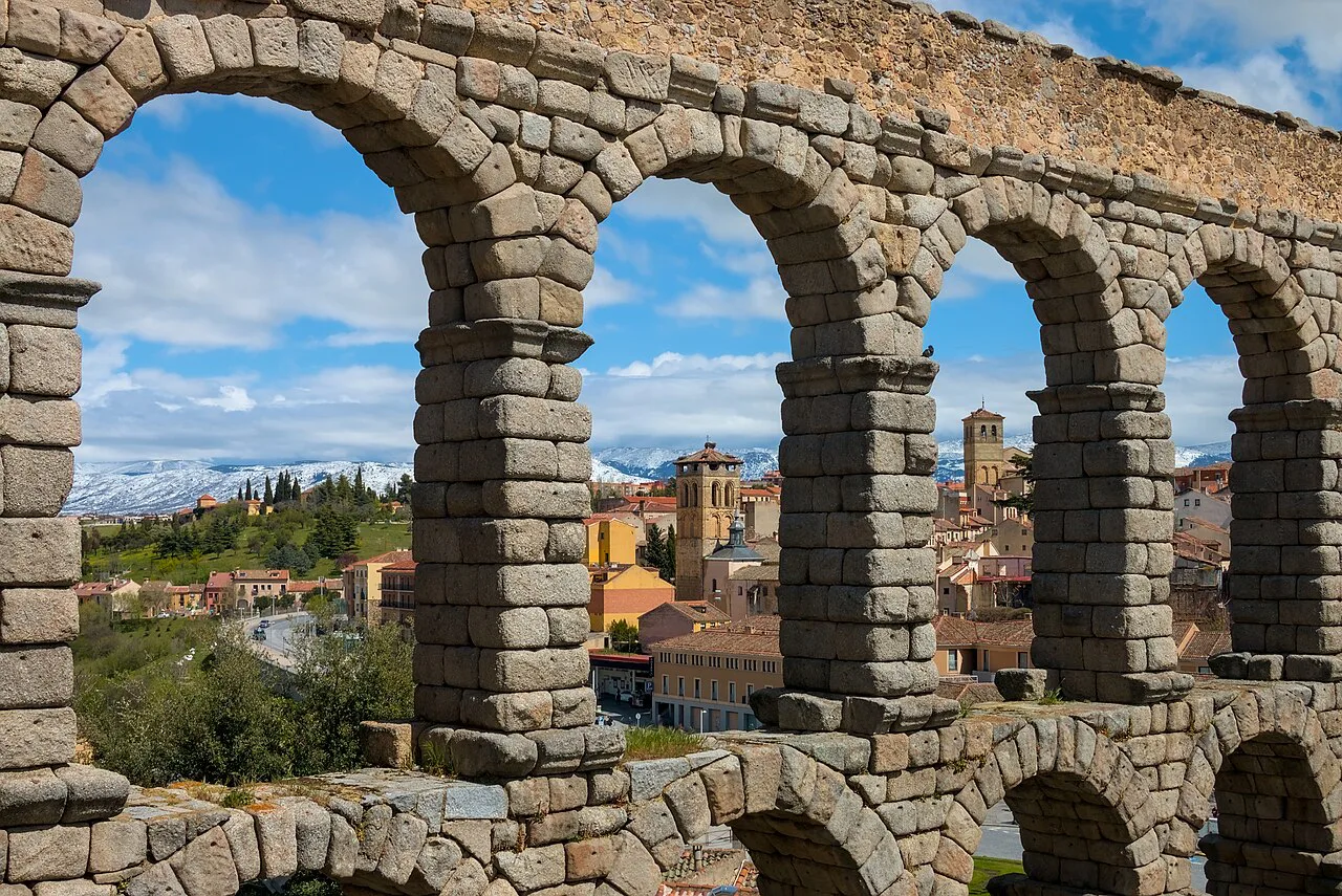 The Roman aqueduct of Segovia framing the town and snowy mountains.